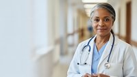 Professional African American female doctor with stethoscope smiling confidently in hospital corridor wearing white medical coat for healthcare concepts.