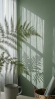 Soft fern shadows cast on a sage green wall with sheer curtains, natural light, and a wicker basket in a calm interior setting.