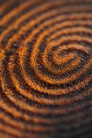 Macro shot of concentric orange and black spiral pattern created with glitter or metallic powder, showing detailed texture and shimmering surface effect.