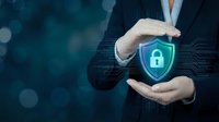 Businessman in dark suit holding green shield with padlock icon, representing cybersecurity protection and data safety for business and technology concepts.