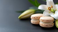 Delicate beige macarons with white lily flowers and buds on dark background, elegant food styling composition for pastry and confectionery advertising.