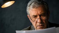 Senior businessman with glasses reading documents under warm lamp light in office setting for corporate and professional presentations.