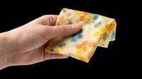 Hand holding beeswax food wrap with honeycomb and bee pattern, isolated on transparent background, ready for eco product clipart, stickers, and print on demand designs.