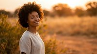 Young African American woman with curly hair enjoying peaceful moment outdoors during golden hour sunset, eyes closed in serene expression for wellness content.