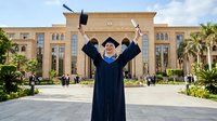 Graduate student in academic regalia celebrating with diploma in front of university building, suitable for education, graduation, and achievement marketing materials.