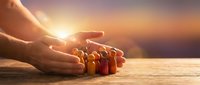 Protective hands cupping wooden family figures at sunset, symbolizing care, security and family protection with warm golden light.