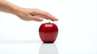 Red apple with human hand touching it on white background, representing fresh produce, healthy eating, nutrition, and organic food selection.