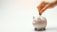 Hand dropping coin into white piggy bank on clean background representing savings and financial planning for future goals.