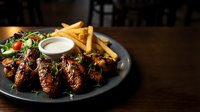 Grilled chicken wings with barbecue glaze served with golden french fries and ranch dipping sauce on dark plate for restaurant menu and food photography.