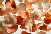 Crispy orange and white prawn crackers scattered on white background, backlit to show texture and translucency. Asian snack food close-up macro photography.