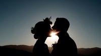 Romantic couple silhouette kissing at sunset with mountain landscape backdrop creating intimate moment for wedding and love themed designs.