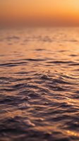 Ocean surface at golden sunset with soft rippling waves and warm orange sky reflecting on calm sea water.