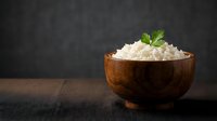 Fresh cottage cheese in wooden bowl with mint garnish on dark background for healthy eating and dairy product concepts.