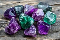 Collection of raw fluorite crystals in purple and green colors scattered on rustic wooden surface for mineral collecting and healing practices.