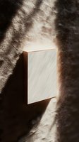 Minimalist wooden frame with blank white canvas on textured wall, illuminated by dramatic natural sunlight casting soft shadows, creating artistic atmosphere.