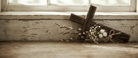Rustic wooden cross with white flowers and rope on weathered windowsill creates peaceful spiritual atmosphere for Easter and religious celebrations.