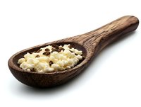 Crushed garlic cloves on rustic wooden spoon against white background, isolated food ingredient for cooking and seasoning preparation.