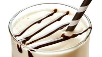 Creamy vanilla milkshake with chocolate syrup drizzle and striped straw in clear glass, perfect for dessert menu photography.