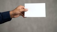 Male hand holding blank white business card against neutral gray background for corporate branding and professional networking purposes.