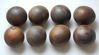 Rustic antique cannonballs arranged in two rows showing aged metal surface with patina and corrosion marks against white background, suitable for historical collections.