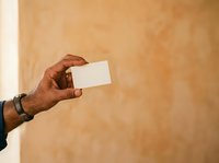 Male hand holding blank white business card against warm beige textured wall background. Suitable for corporate branding, business identity, and professional marketing materials.
