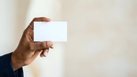 Male hand with dark skin tone holding blank white business card against neutral beige background, suitable for corporate branding, identity design, and professional marketing materials.