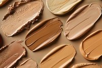 Makeup foundation smears in different skin tone shades on beige background, showing texture and variety of cosmetic product swatches for beauty industry.