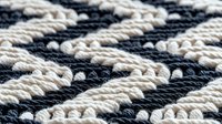 Diagonal striped pattern made of twisted cotton rope in black and white creates nautical macrame texture. Close up view shows woven textile detail.