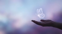Silhouette of open palm releasing translucent butterfly against dreamy purple and blue gradient sky background symbolizing freedom and transformation.