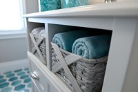 Organized bathroom storage with wicker baskets containing folded teal towels in white wooden shelving unit for home organization and interior design.