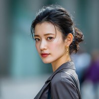 Young Asian businesswoman with elegant updo hairstyle and gold earrings in professional attire looking confidently at camera in modern office setting.