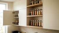 Organized kitchen cabinetry with open wooden shelves displaying glass jars and spice containers, white cabinet doors, and neutral tones for home interior design and kitchen storage solutions.