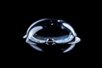 Water droplet with perfect spherical shape creating ripples on liquid surface against black background for science and nature concepts.