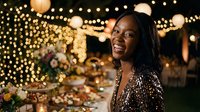 Happy African American woman smiling at elegant evening party with warm string lights and floral decorations creating festive celebration atmosphere.