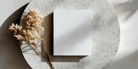 Minimalist white card mockup on textured stone plate with dried flowers and soft shadows for elegant branding presentation.