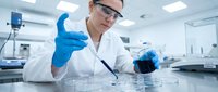 Female scientist in blue gloves examining dark liquid sample in modern laboratory. Professional researcher conducting chemical analysis in sterile environment.
