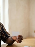 Young African male with dark skin tone holding blank white business card in hand at wooden table, suitable for corporate branding and professional networking materials.