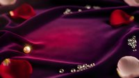 Luxurious purple velvet fabric with elegant golden beads and rose petals creating romantic atmosphere for fashion design and textile projects.