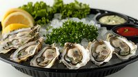 Fresh raw oysters served on ice with lemon slices, parsley garnish and dipping sauces in black serving platter, closeup view of luxury seafood appetizer.