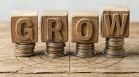 Wooden blocks spelling GROW stacked on increasing coin piles representing financial growth and investment success on rustic wood surface.