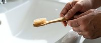 Elderly man holding a bamboo toothbrush over a white sink, promoting eco-friendly oral hygiene and sustainable bathroom routines.