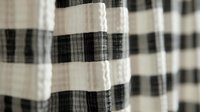 Textured black and white gingham pattern on seersucker fabric with soft pleats and natural folds creating depth and dimension, suitable for fashion and interior design backgrounds.