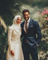 Happy Muslim couple in elegant wedding attire smiling together outdoors with natural garden background for celebration and romance concepts.