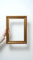 Hand holding ornate golden picture frame against white wall background for art display, home decor, gallery presentation and interior design projects.