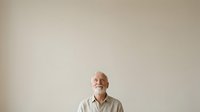 Senior man with white beard and gray hair wearing light beige button-up shirt, smiling while looking upward against neutral background for portrait and lifestyle use.