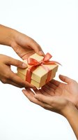 Two hands passing a gold gift box with red ribbon, symbolizing giving, generosity, and celebration on a white background.