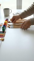 Female artist hands organizing wooden paintbrushes on white desk with watercolor paints and coffee mug in bright creative workspace for art projects.