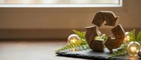 Wooden recycling symbol with golden Christmas ornaments and pine branches on tablet screen, representing sustainable holiday practices and eco-friendly celebrations.