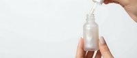Hand applying clear serum from dropper bottle onto palm against clean white background for skincare routine and cosmetic product demonstration.