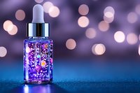 Glowing purple serum dropper bottle with sparkles on blue surface against blurred bokeh background, cosmetic skincare product photography for beauty industry.